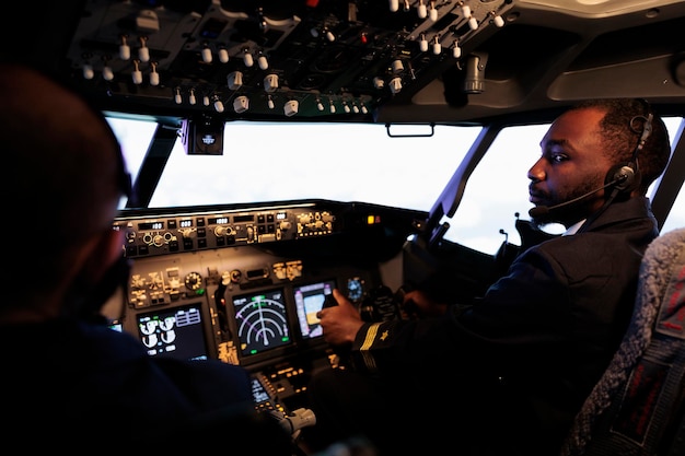 Piloto americano africano voando jato de aeronaves fazendo trabalho em equipe com o capitão, usando o comando do painel e navegação. Equipe de aviões empurrando os botões do painel de controle e alavanca para decolar e voar.