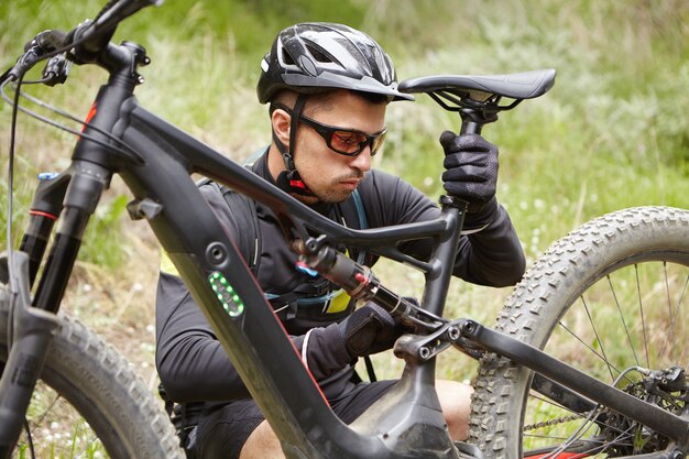 Piloto caucasiano usando equipamento de proteção ajustando o assento de sua bicicleta movida a bateria