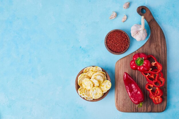 Pimenta vermelha fatiada e pimentão em uma bandeja de madeira servida com batatas fritas, vista superior.