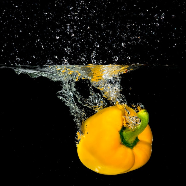 Pimentão amarelo fresco cair na água com um respingo e bolha de ar