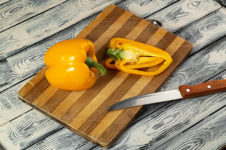 Foto grátis pimentão amarelo fresco maduro e fatiado na mesa de madeira marrom e fundo cinza