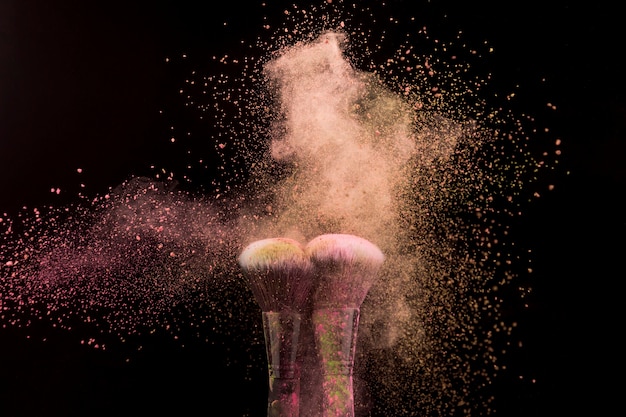 Foto grátis pincéis de maquiagem em explosão de pó bege em fundo escuro