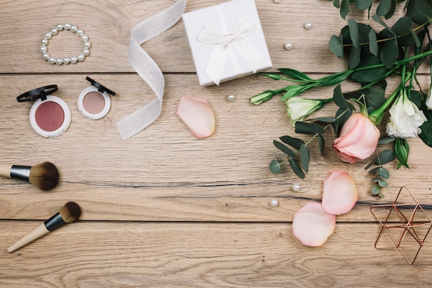 Pincel de maquiagem; pó facial compacto; pérolas; caixa de presente; rosa e eustoma flores na mesa de madeira