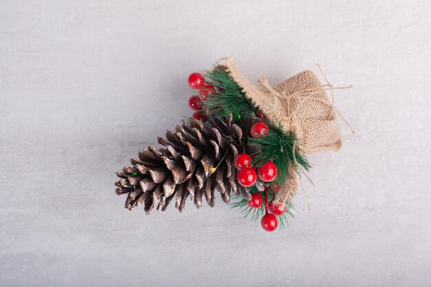 Pinha decorada com bagas de azevinho e floco de neve na mesa branca.