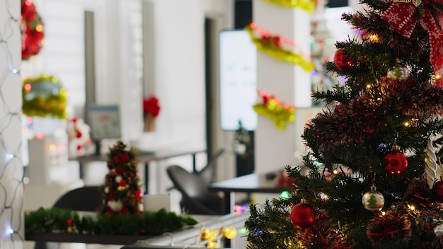 Foto grátis pinheiro de natal adorna com guirlandas e enfeites no escritório vazio. previsões de receitas de negócios em telas de computador no natal adornam locais de trabalho sem trabalhadores durante as férias de inverno