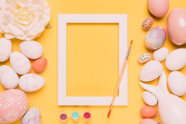 Pintar cor; pincel; moldura de borda branca; rosa e ovos de Páscoa no pano de fundo amarelo