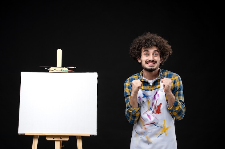 Foto grátis pintor frontal com cavalete segurando uma figura humana de brinquedo na parede preta
