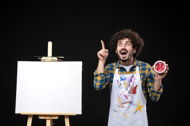 Foto grátis pintor masculino com cavalete segurando relógios na parede preta