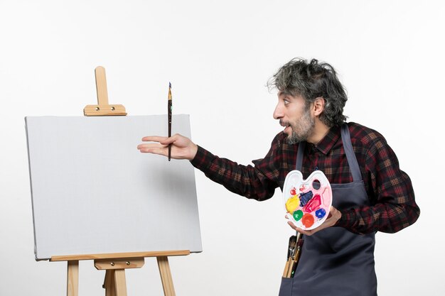 Pintor masculino se preparando para desenhar com tintas e pincel em uma parede branca