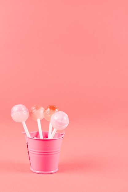 Foto grátis pirulitos doces no balde pequeno rosa contra fundo coral