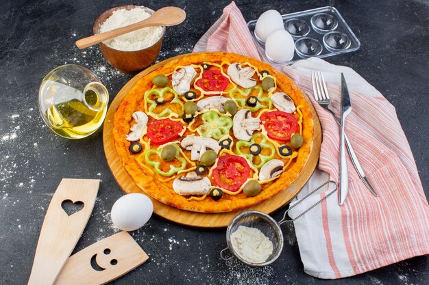 Pizza de cogumelos apimentados com tomates vermelhos, pimentões azeitonas, tudo fatiado dentro com óleo e farinha na mesa cinza.