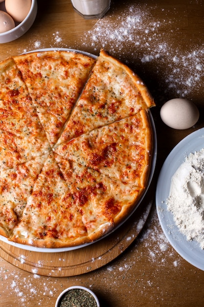 Foto grátis pizza de queijo com tomate e especiarias fatiadas na mesa de madeira