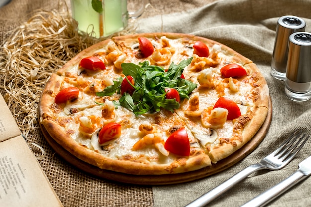 Pizza de vista lateral com camarão e cogumelos tomates e rúcula e com um refrigerante