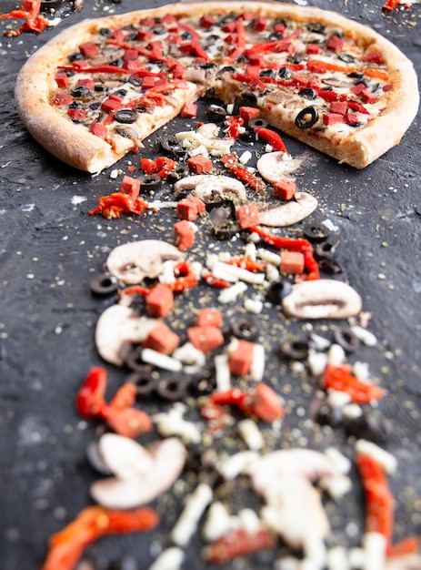 Pizza em fatias e cogumelos, pimenta vermelha e azeitonas em uma placa de pedra preta