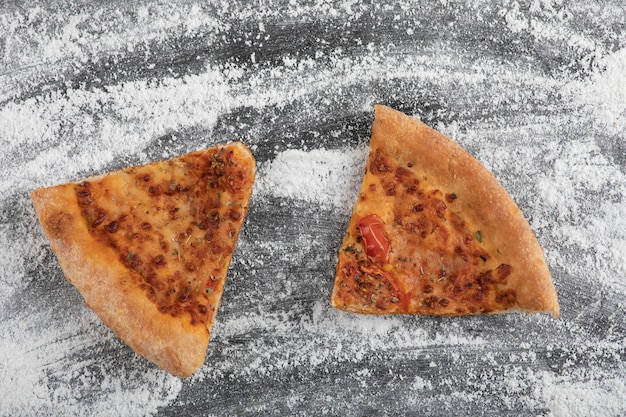 Pizza fatiada caseira na superfície preta com farinha de trigo derramada