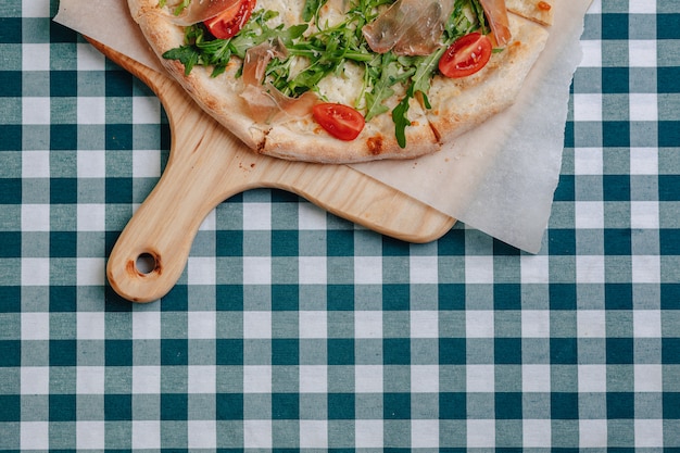 Pizza napolitana com salame, rúcula, tomate polvilhado com queijo em uma placa de madeira em uma toalha de mesa em uma célula