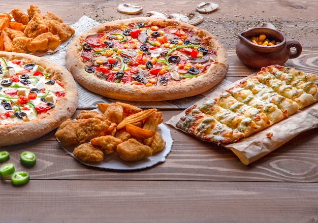 Pizzas, churrasco de frango, batatas fritas e rolinhos de queijo na mesa de madeira