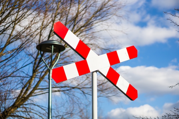 Placa de cruzamento de ferrovia contra árvores nuas e céu azul nublado