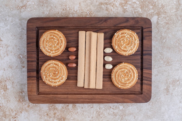 Placa de madeira com deliciosos biscoitos crocantes na superfície de mármore.