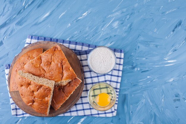 Placa de madeira com fatias de pão, gema de ovo e farinha na superfície azul.