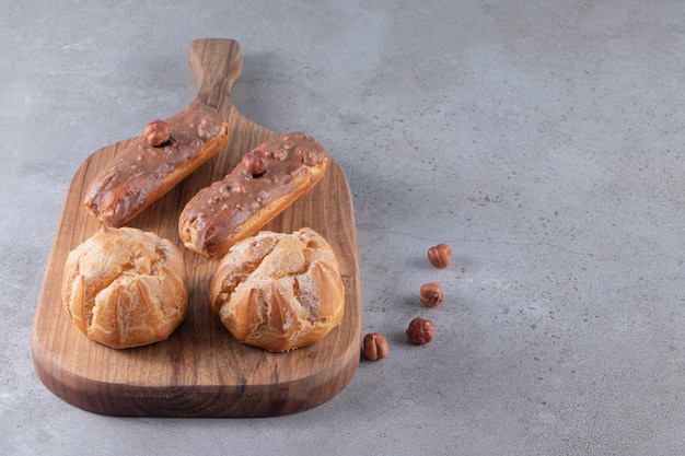 Placa de madeira de doces profiteroles e éclairs na mesa de pedra.