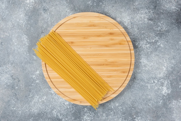 Placa de madeira de espaguete seco cru colocado na superfície de mármore.