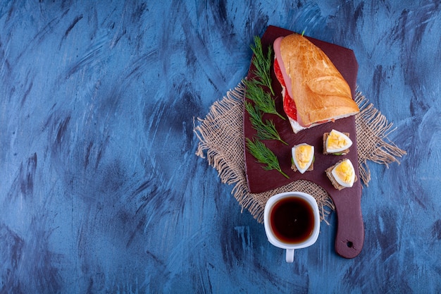 Placa de madeira de sanduíche caseiro fresco com uma xícara de chá quente.