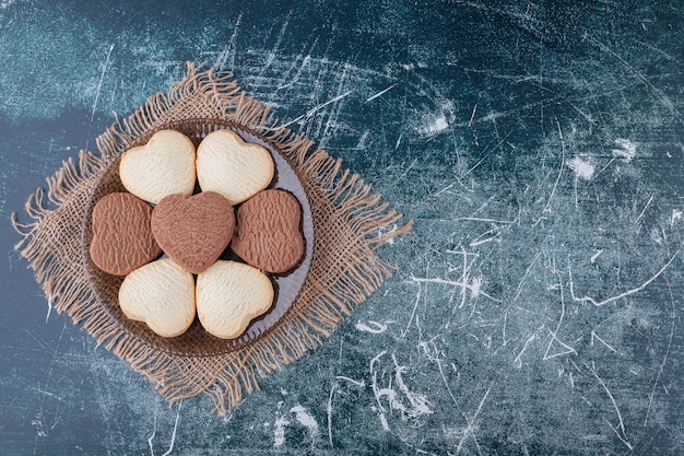 Placa escura de biscoitos em forma de coração colocados sobre fundo de mármore.