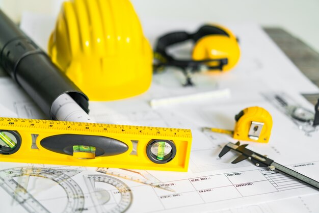 Planos de construção com capacete e ferramentas de desenho em plantas.