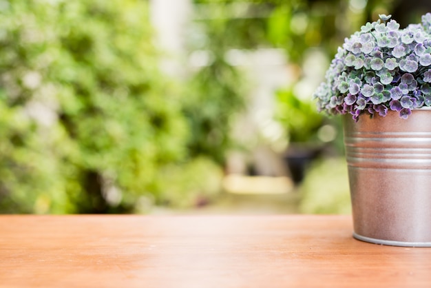 Planta verde em um potenciômetro de flor em uma mesa de madeira na frente da casa com o fundo borrado da textura do jardim.