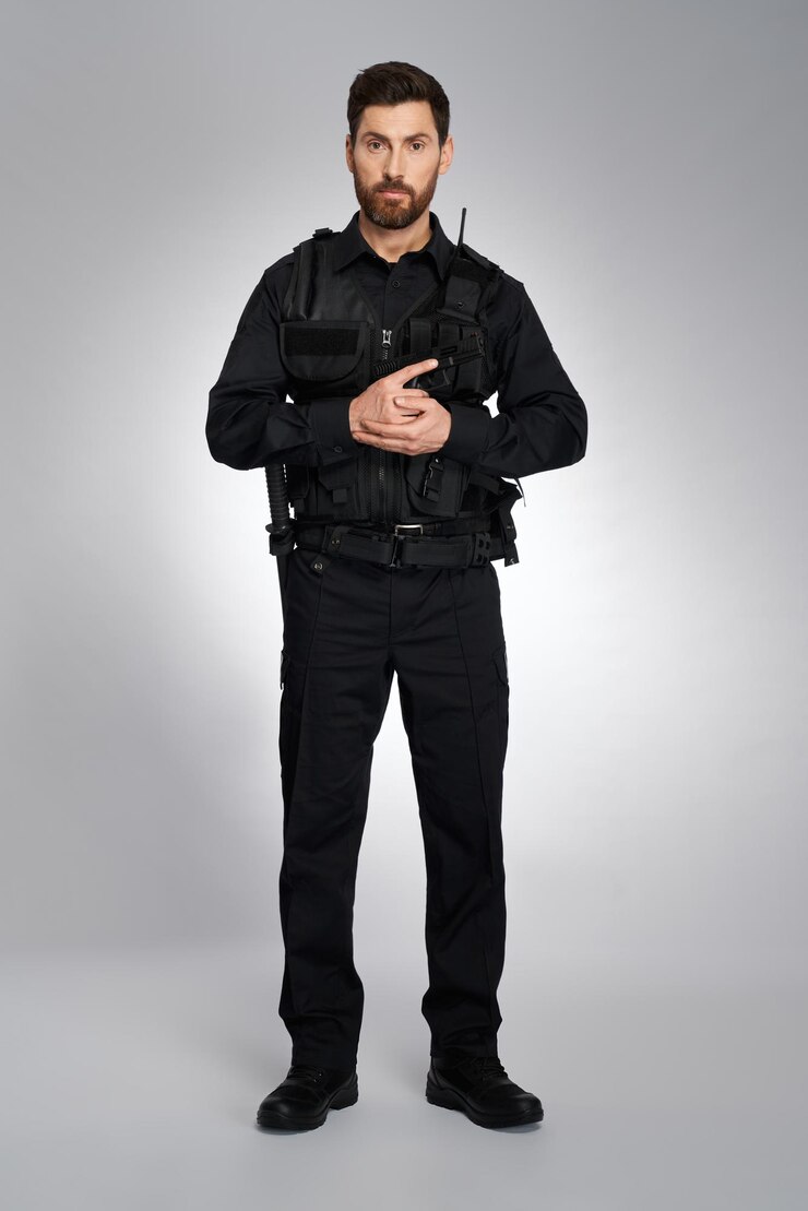 Foto grátis policial masculino atraente com munição segurando arma com ambas as mãos vista frontal do homem barbudo de preto