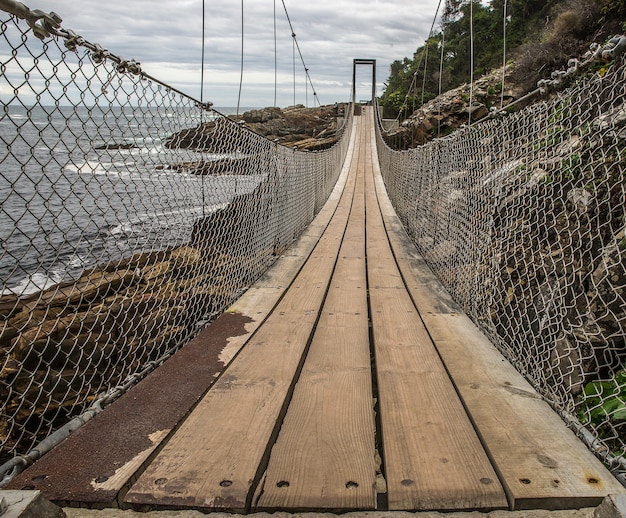 Ponte feita de madeira e metal contornando a montanha ao lado da praia