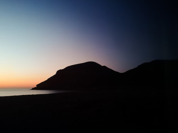 Pôr do sol com uma montanha de silhueta na praia