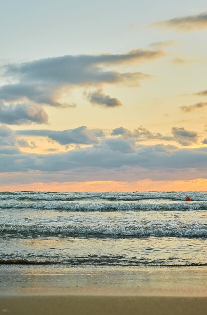 Pôr do sol da praia de areia sobre o mar com nuvens coloridas luz solar laranja Quadro vertical pôr do sol do outono no início do outono temporada de veludo A ideia de um plano de fundo ou tela inicial