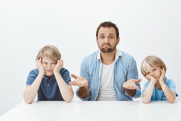 Por que os filhos estão loucos. Retrato do sogro nervoso sem noção sentado com dois meninos bonitos à mesa