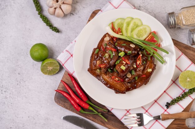 Porco doce em um prato branco com cebolinha picada, pimenta, limão, pepino, tomate e alho.