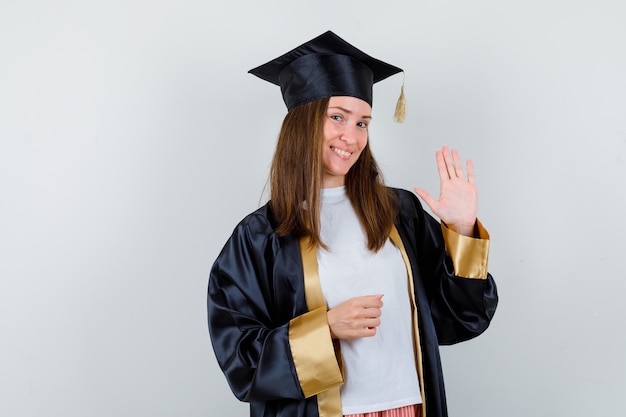 Foto grátis pós-graduação feminino acenando com a mão para saudação em roupas casuais e uniformes e olhando alegre, vista frontal.