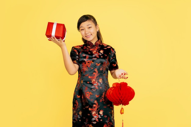 Posando com lanterna e presente, sorrindo. feliz ano novo chinês 2020. retrato de uma jovem asiática sobre fundo amarelo. modelo feminino com roupas tradicionais parece feliz. celebração, emoções. copyspace.