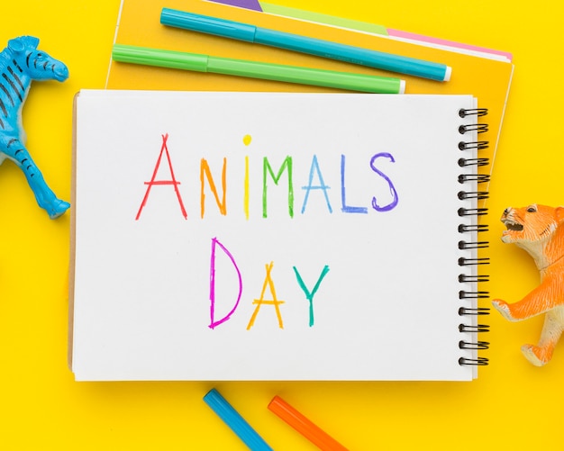 Posição plana de estatuetas de animais e escrita multicolorida no caderno para o dia dos animais