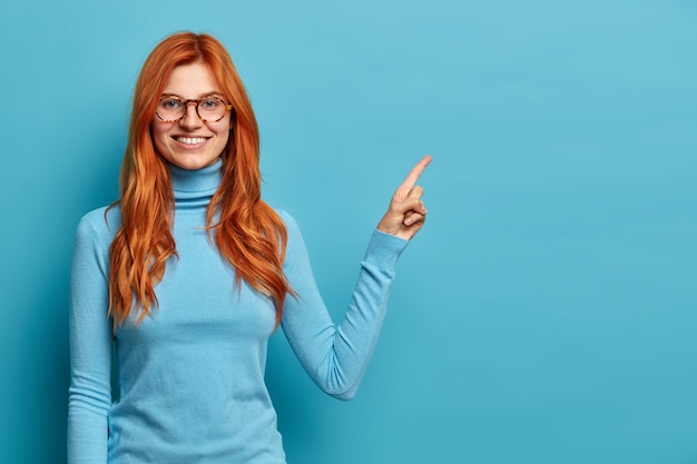 positiva ruiva bonita olhando mulher caucasiana com sorriso dentuço aponta no espaço da cópia no canto superior direito.