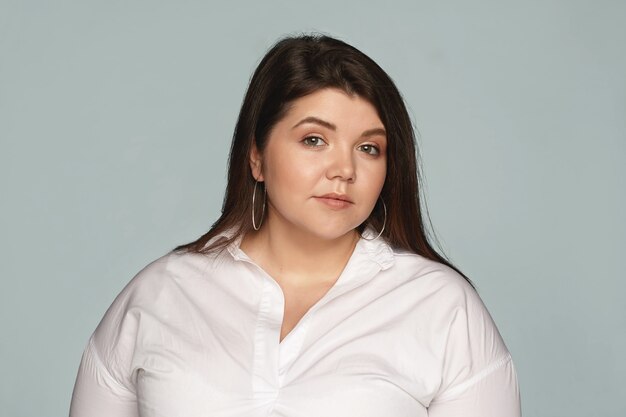 Positividade corporal, feminilidade, beleza, cosmética e conceito de moda. Foto de uma linda jovem gordinha atraente, vestida com uma camisa branca, posando