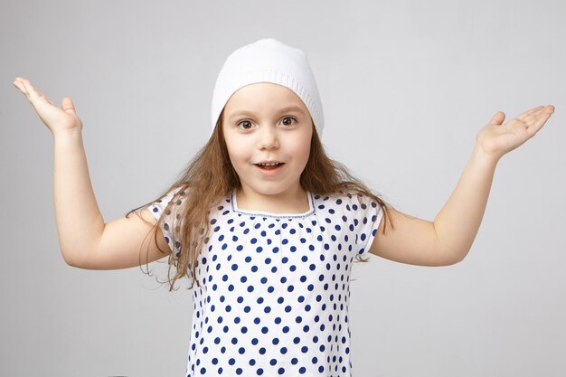 Positivo, fascinado, menina de 5 anos de idade com chapéu e camiseta levantando as mãos