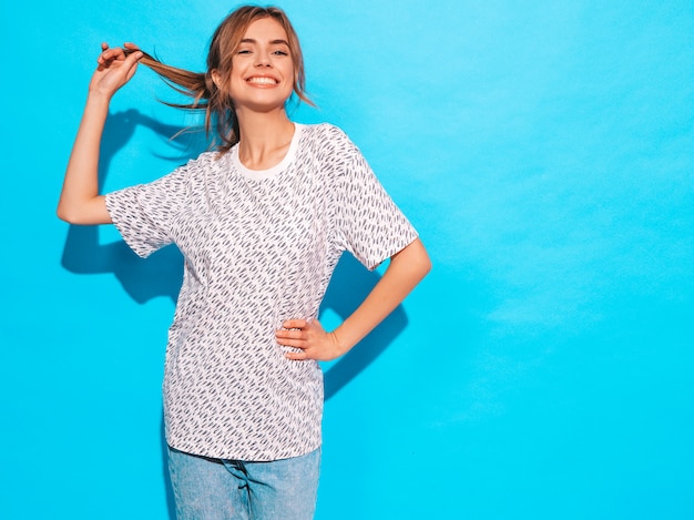 Positivo feminino sorrindo. Modelo engraçado posando perto da parede azul no studio.Ela toca o cabelo dela