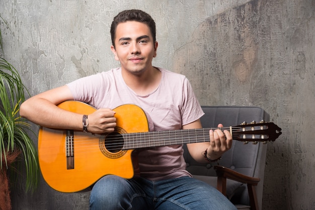 Positivo jovem sentado na cadeira e tocando violão.