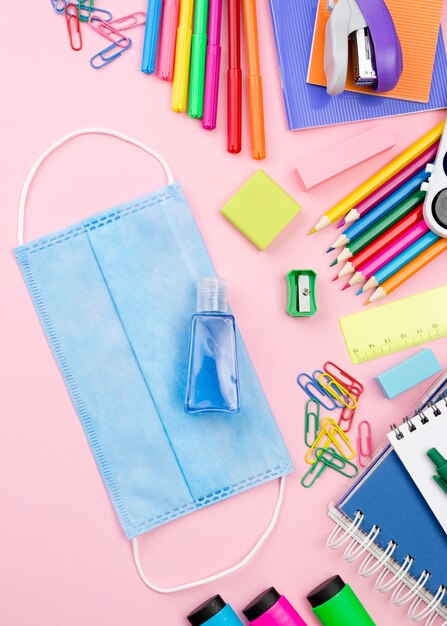 Postura plana de colorido de volta aos artigos de papelaria da escola com máscara médica