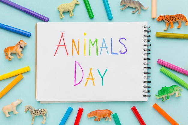 Postura plana de estatuetas de animais e escrita colorida no caderno para o dia dos animais