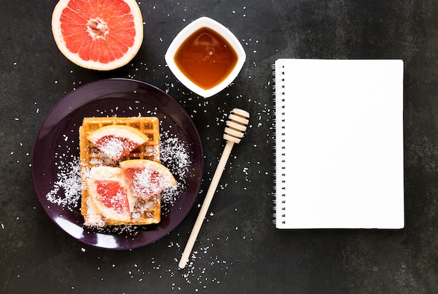 Foto grátis postura plana de notebook com prato de waffles e frutas cítricas