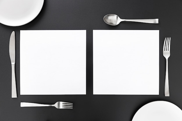 Postura plana de papéis de menu em branco com talheres e pratos