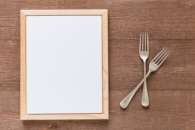 Postura plana de papel de menu em branco com talheres na superfície de madeira