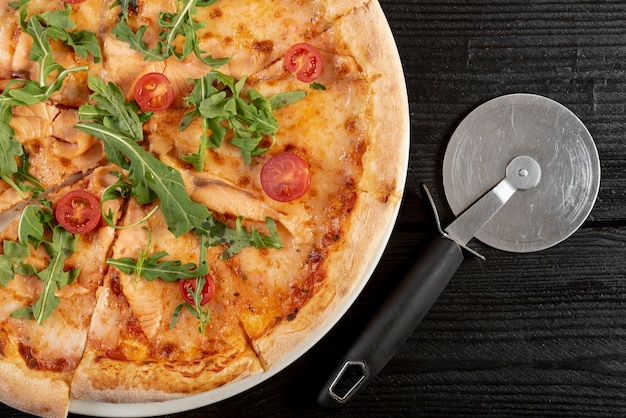 Postura plana de pizza com rúcula e tomate cereja na mesa de madeira